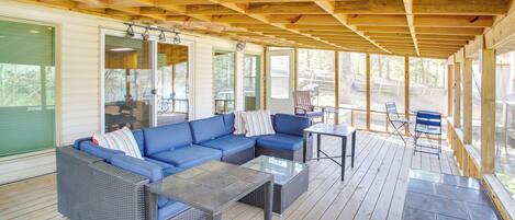 Un espace extérieur abrité comprenant un canapé d’angle bleu, deux tables avec plateaux en verre et une terrasse en bois.