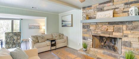 A living room with a stone fireplace, a ceiling fan, and a sofa with cushions.