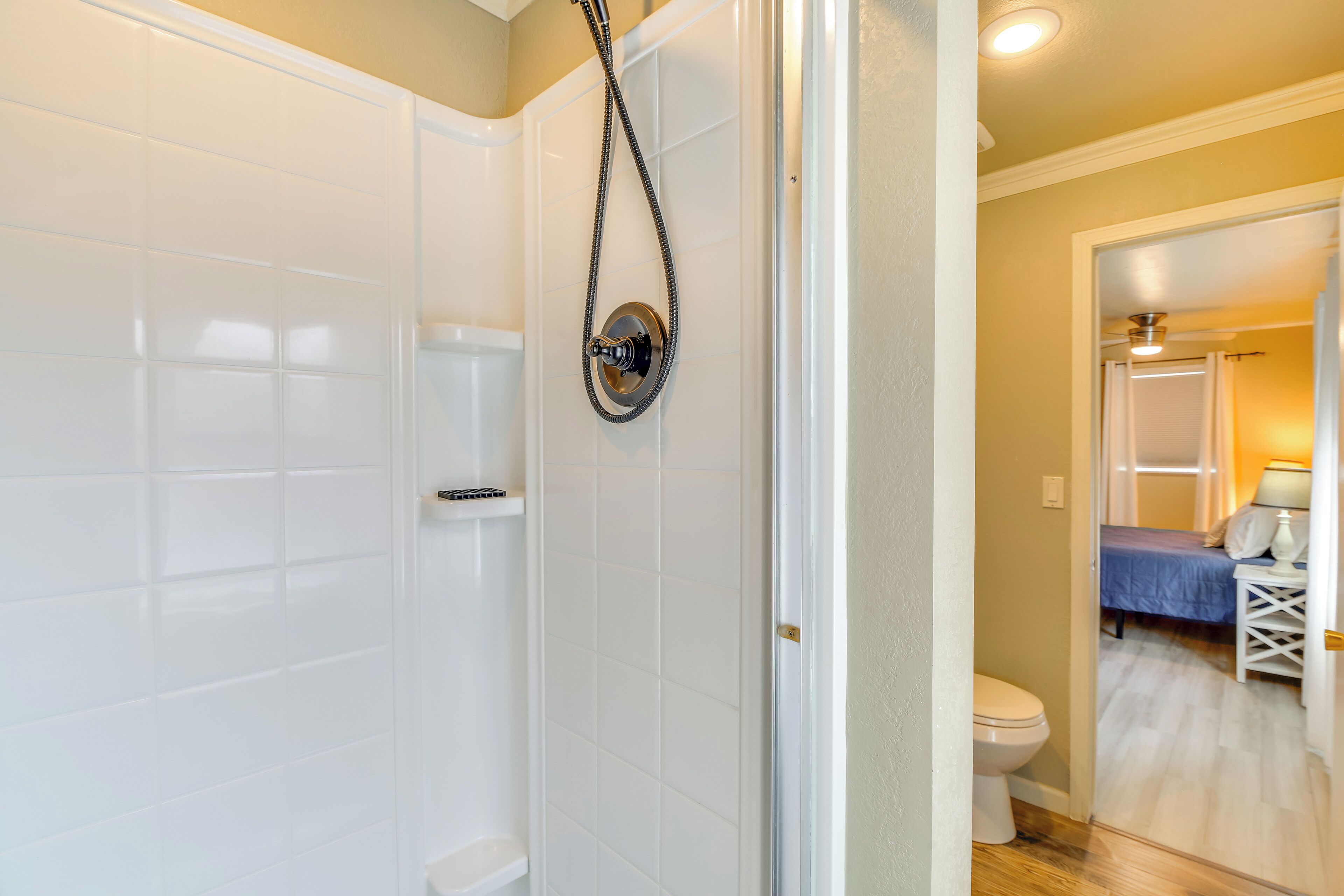 Bagno con piastrelle bianche, doccia con soffione a mano e water visibile.