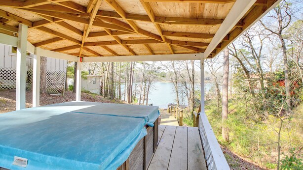 A covered outdoor area with a wooden deck and a blue tarp-covered object, likely a pool or hot tub, with a view of a body of water and trees in the background.