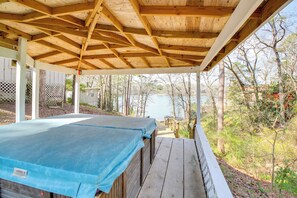 Un'area esterna coperta con un pavimento in legno e un oggetto ricoperto da un telo blu, probabilmente una piscina o una vasca idromassaggio, con vista su un corpo d'acqua e alberi sullo sfondo.