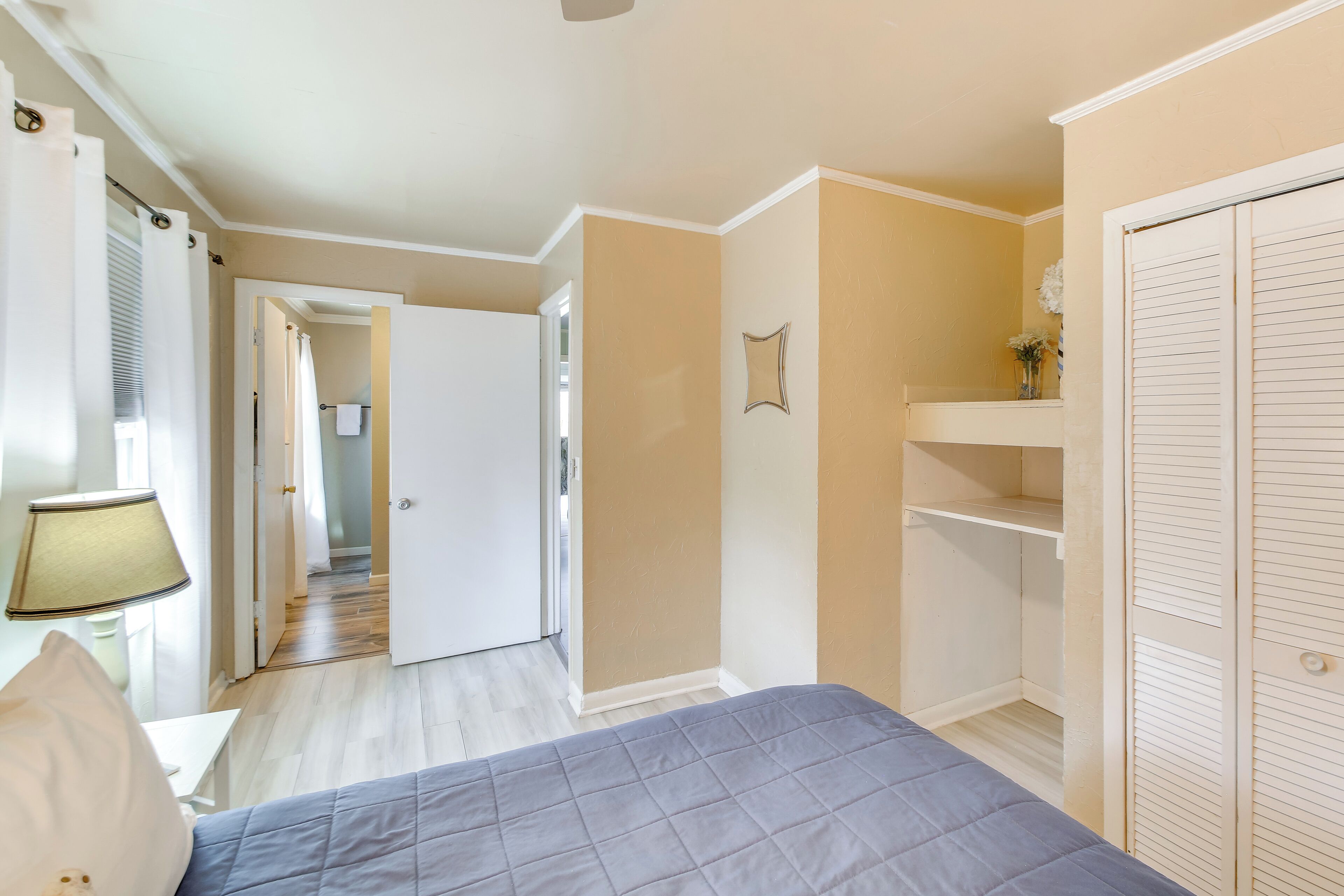 A bedroom with a bed, a nightstand, a lamp, a wardrobe, and a door leading to another room.