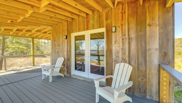 Eine Holzterrasse mit zwei weißen Adirondack-Stühlen und einer Glastür, die zu einem Außenbereich führt.
