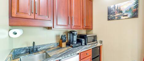 A kitchen with wooden cabinets, a marble countertop, a sink, a refrigerator, a microwave, and a painting on the wall.
