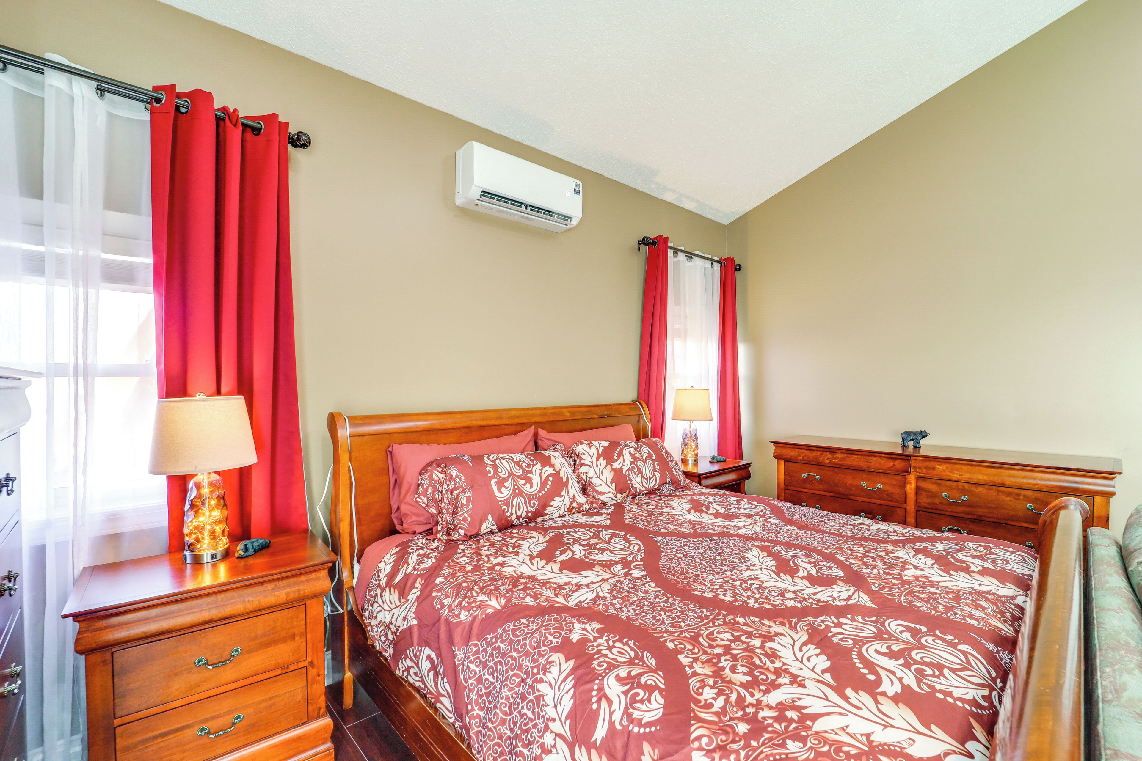 A bedroom with a wooden bed, red curtains, a nightstand with a lamp, and a dresser.