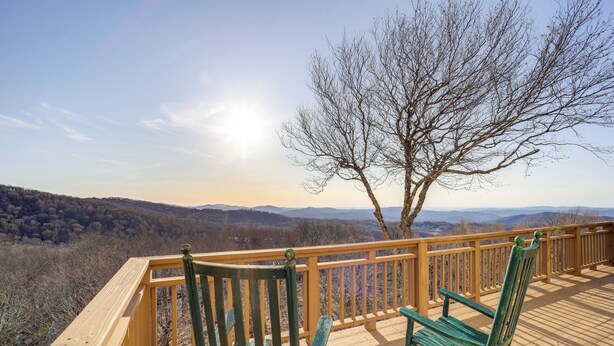 Eine Holzterrasse mit zwei grünen Stühlen und Blick auf eine bewaldete Landschaft.