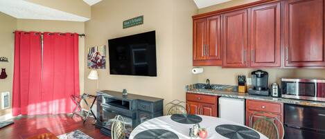 A modern kitchen with red cabinets, a flat-screen TV, and a dining area with a round table and placemats.