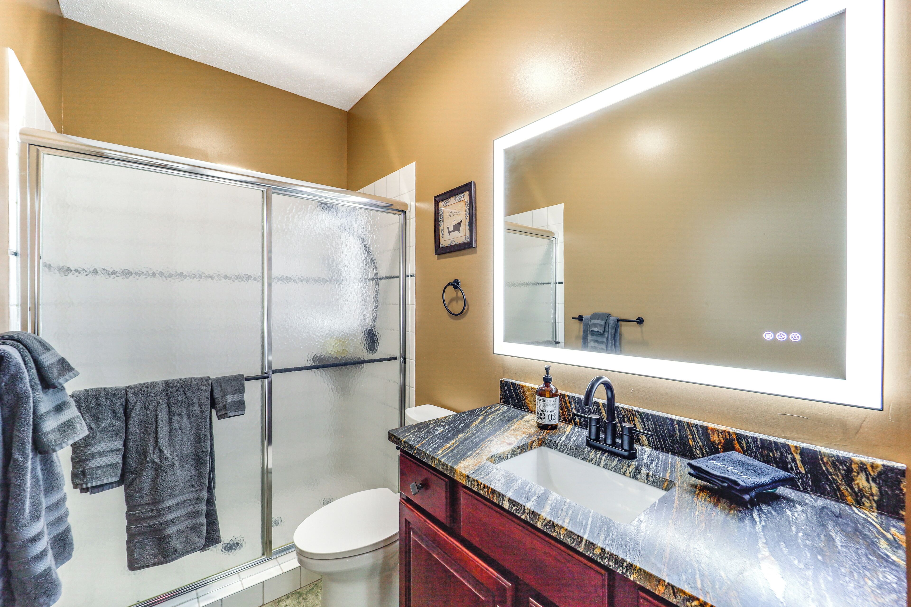 A bathroom with a glass shower enclosure, a white toilet, a marble sink with a black faucet, and a large mirror.