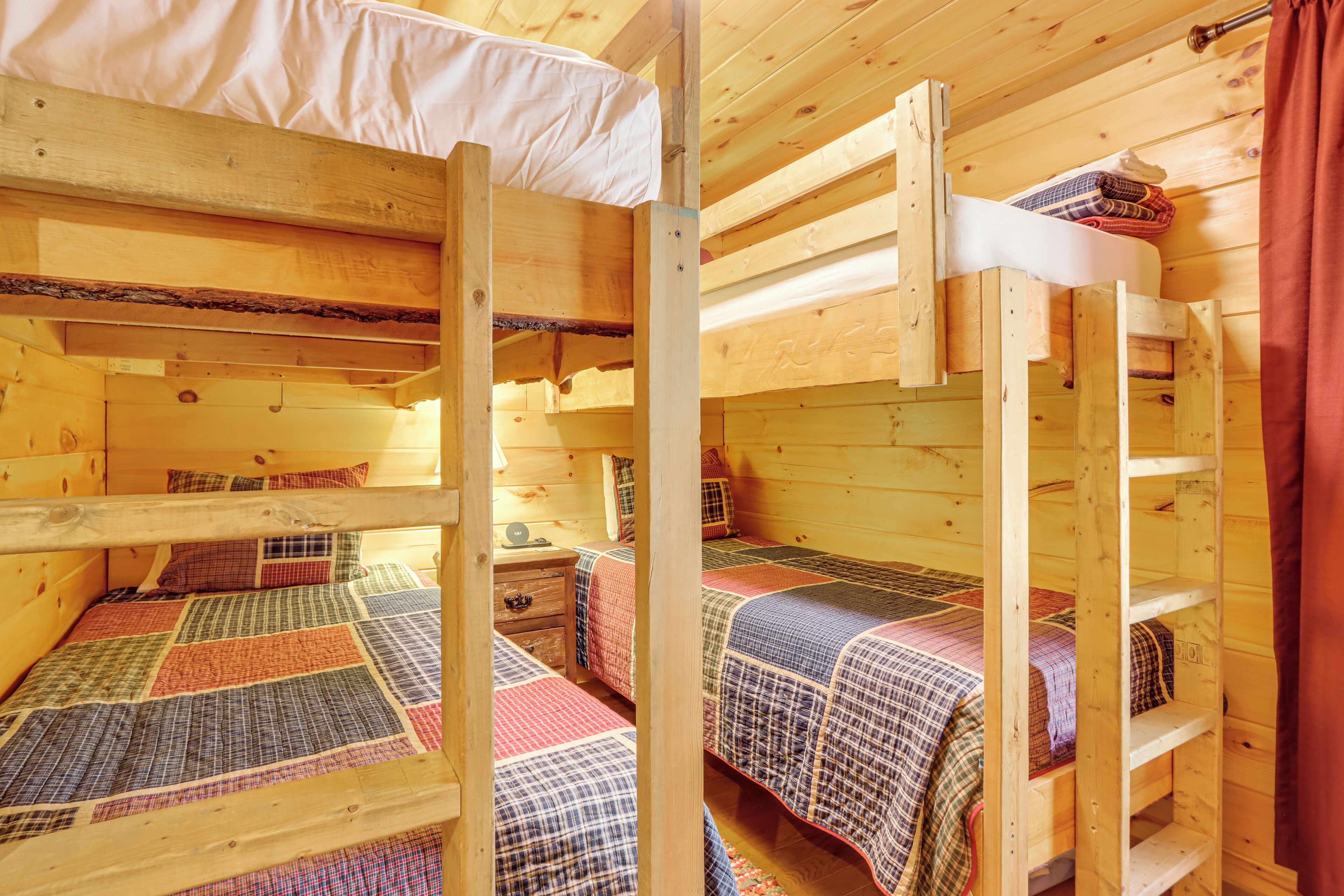 Una cabaña con tres literas, cada una con una colcha acolchada. Hay un aparador de madera y una mesita con una lámpara.