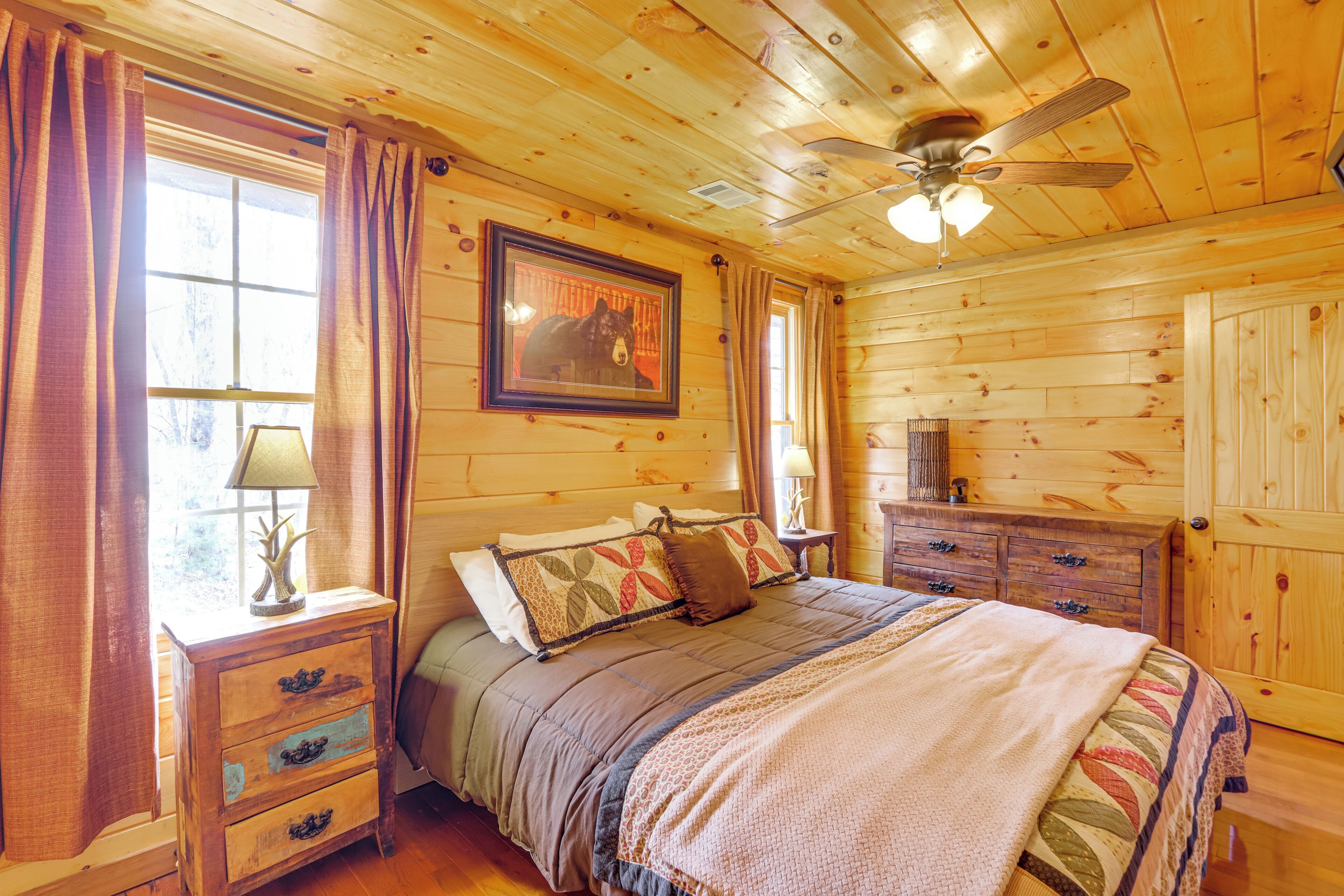 A wooden cabin bedroom with a bed, nightstands, a dresser, and a ceiling fan.