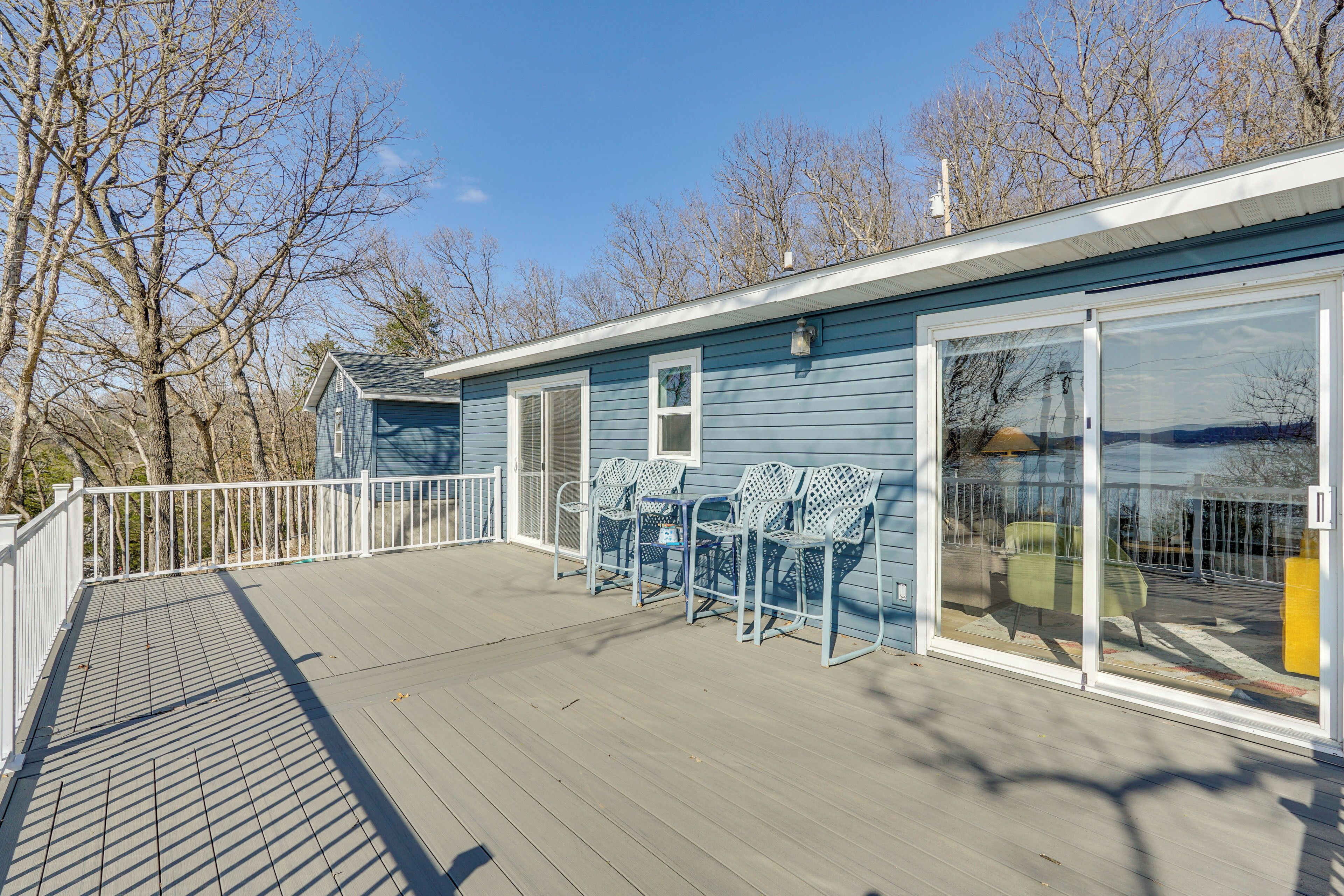 A blue building with a covered deck, white railing, and metal chairs.