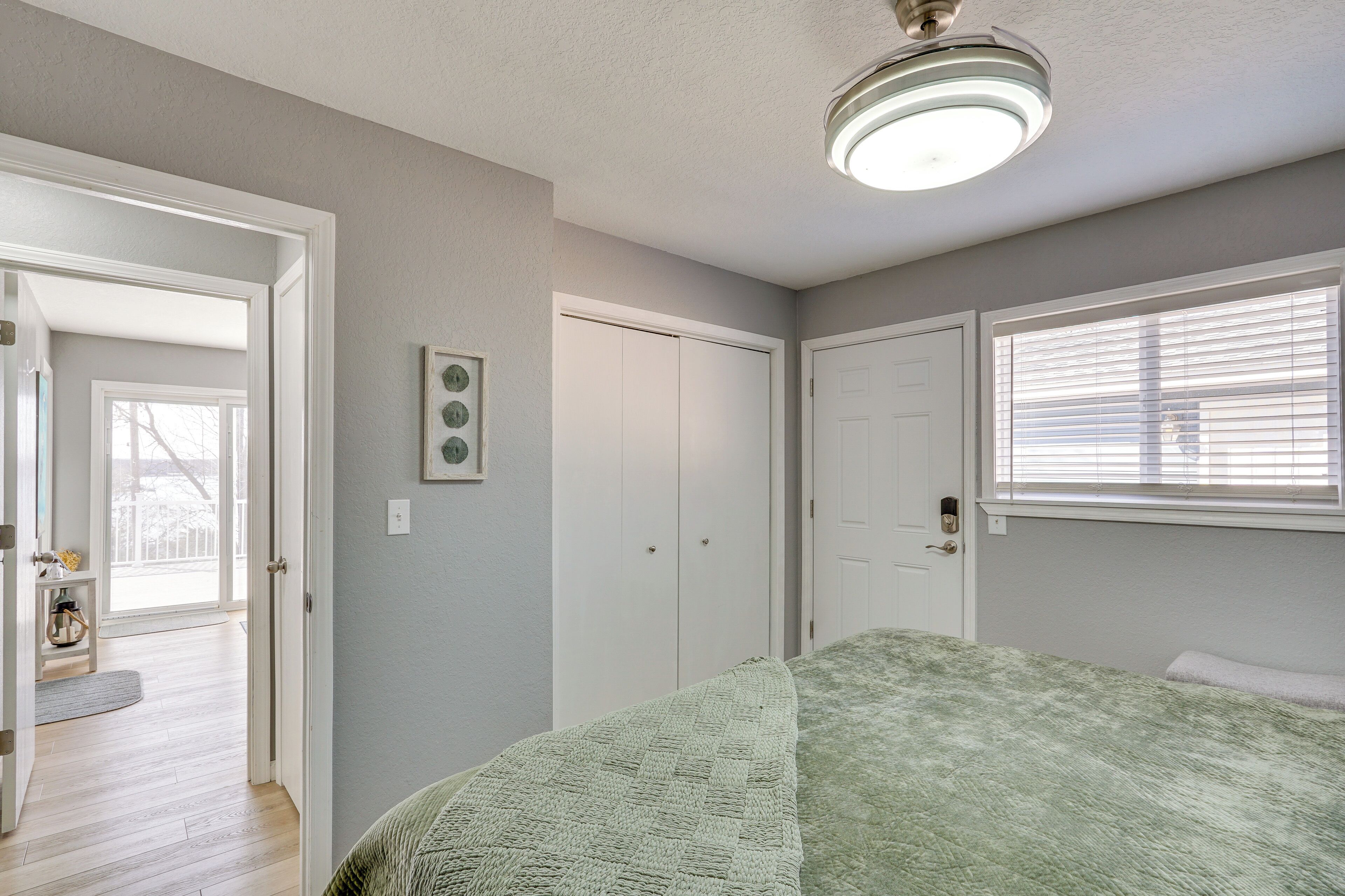 Une chambre à coucher avec un lit, une porte, une fenêtre avec des stores et un luminaire au plafond.