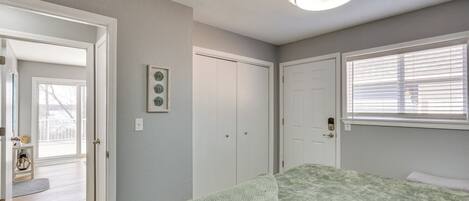 Une chambre à coucher avec un lit, une porte, une fenêtre avec des stores et un luminaire au plafond.
