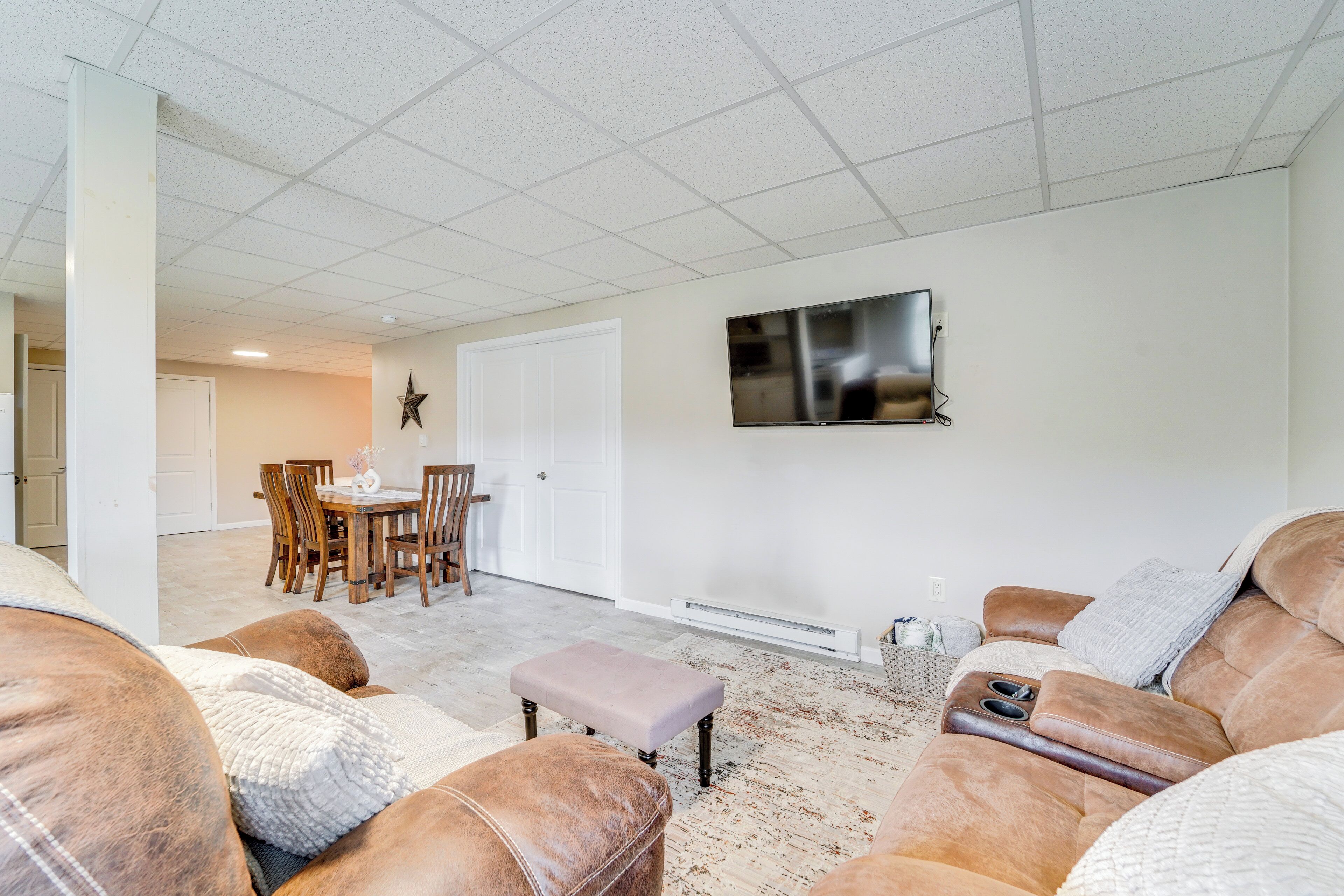A spacious living room with a large sectional sofa, a dining area with wooden chairs, and a flat-screen TV mounted on the wall.