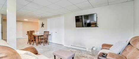 A spacious living room with a large sectional sofa, a dining area with wooden chairs, and a flat-screen TV mounted on the wall.