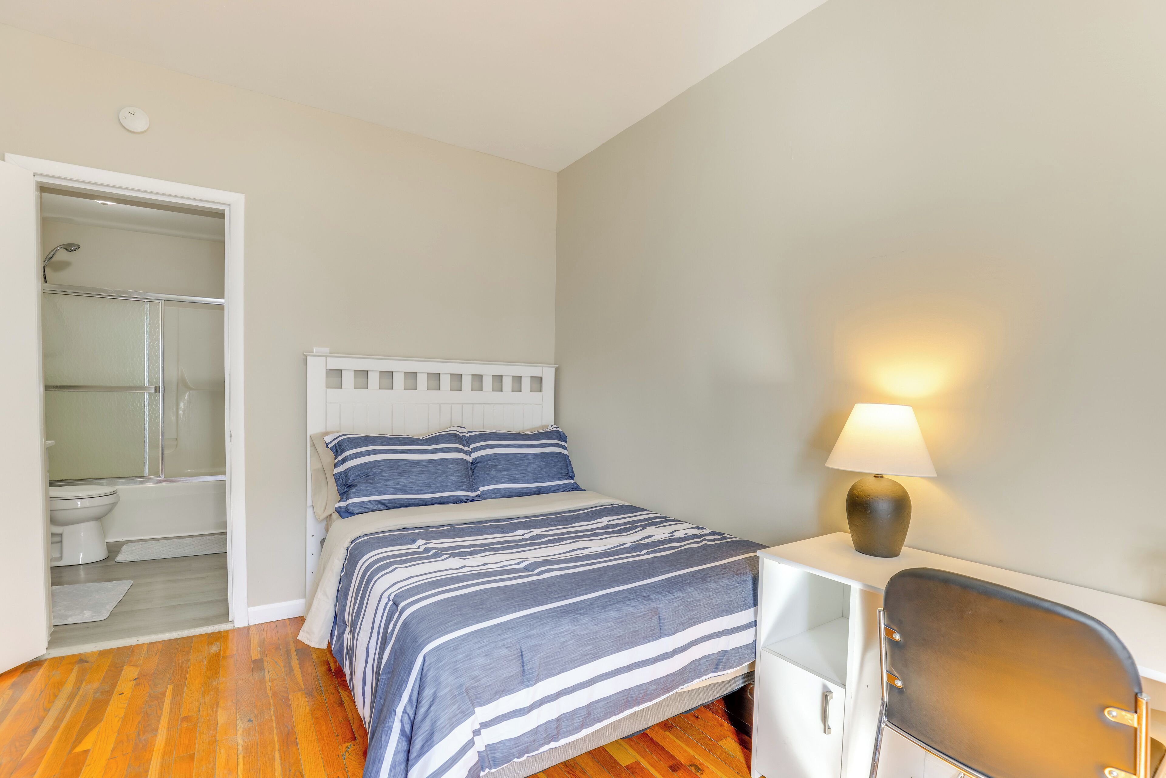 Une chambre à coucher comprenant un lit, une table de chevet avec une lampe, une chaise et un dressing avec une douche.