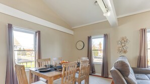 A dining area with a wooden table and chairs, a clock on the wall, and a couch in the background.