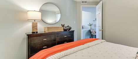 A bedroom with a bed, a dresser, a lamp, a mirror, and a door leading to another room.