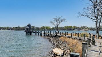 A wooden pier leading to a gazebo by a calm lake, with a boat on the shore and a clear sky.