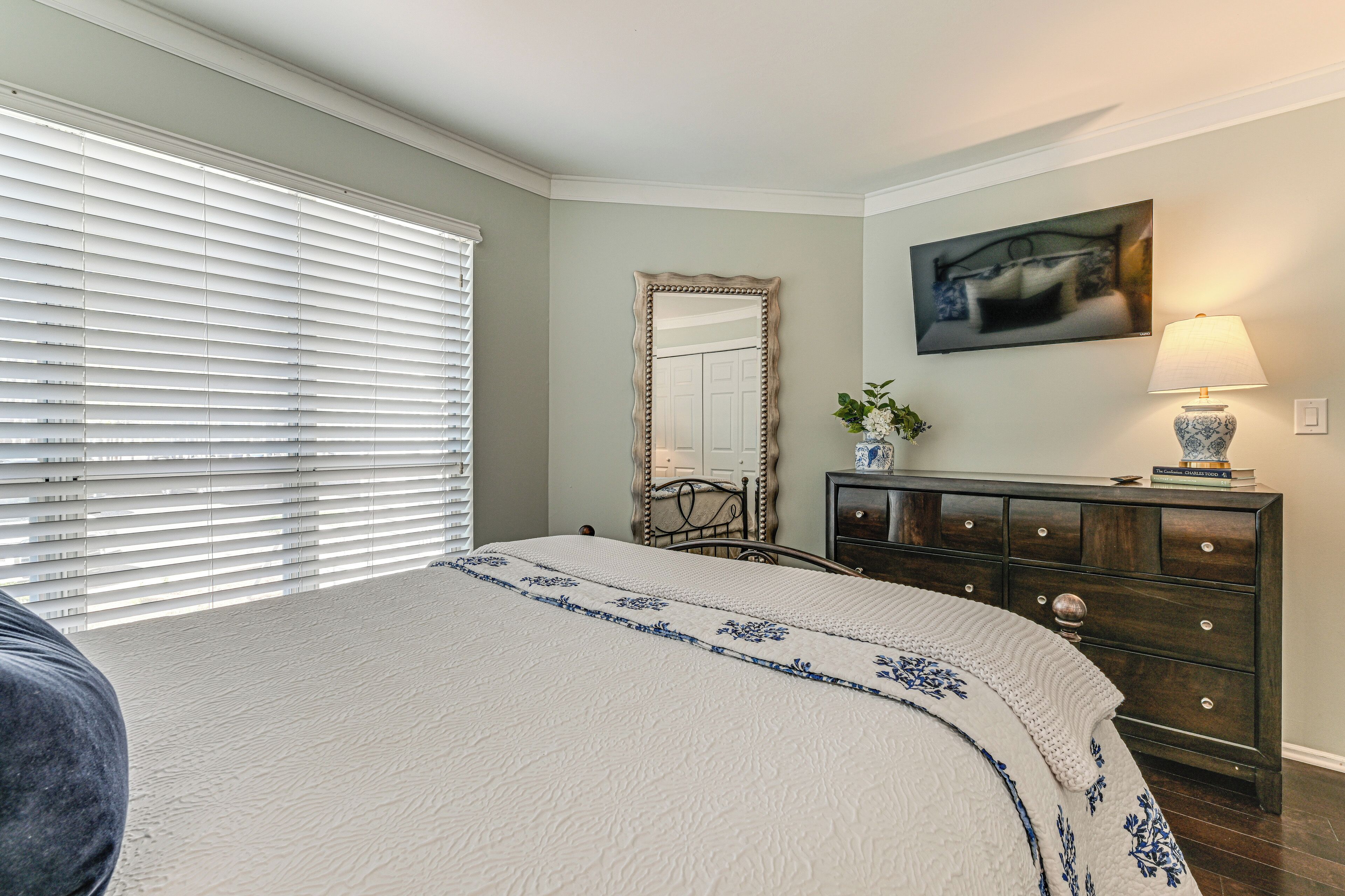 A bedroom with a bed, a dresser, a mirror, and a painting on the wall.