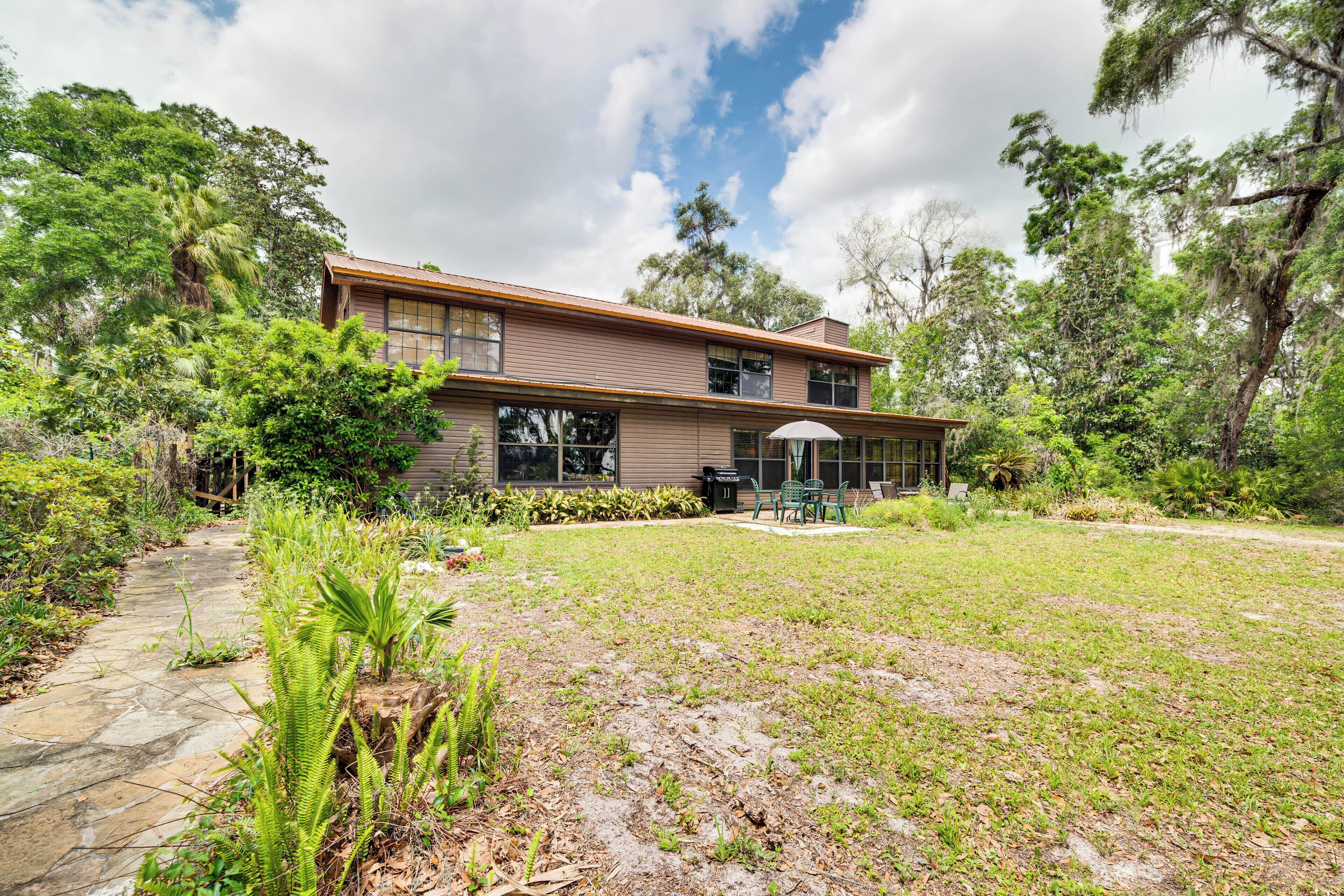 A two-story house with a stone pathway leading to the entrance, surrounded by lush greenery and trees.