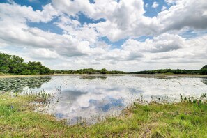 A natural landscape with a body of water, grassy areas, and trees under a partly cloudy sky.