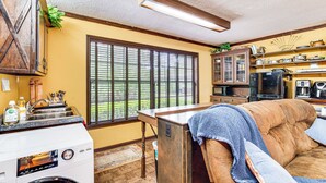 A compact kitchen with a washing machine, a dining area with a sofa, and a large window with blinds. - Lake Access + Private Patio: Sunny Inverness Apt! (Inverness)