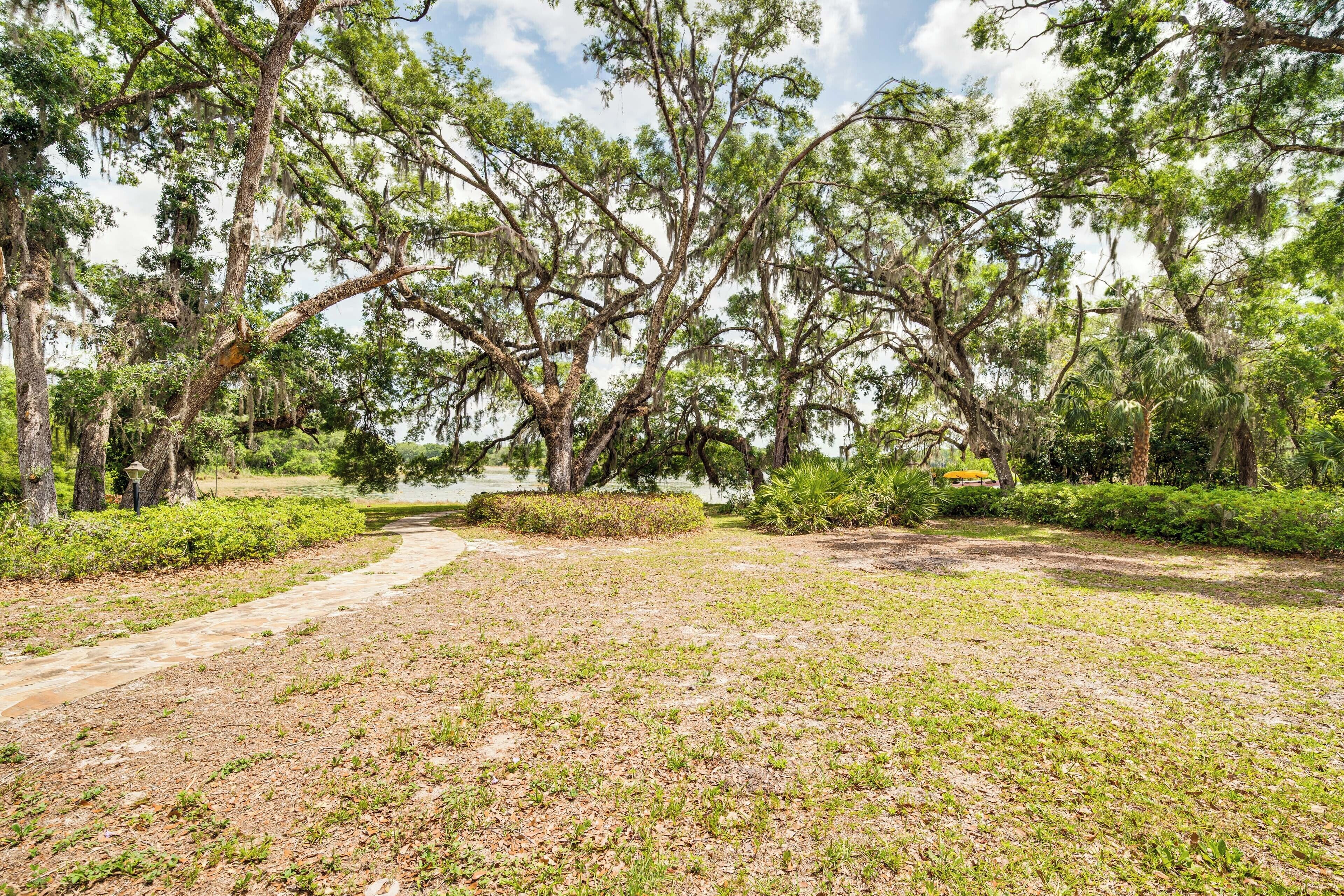 A park with a dirt path, trees, and a body of water in the background.