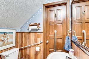 A bathroom with wooden paneling, a toilet, a sink, a mirror, a towel rack, and a picture on the wall.