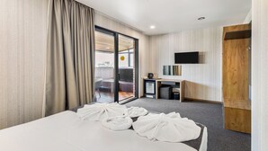 Et hotelværelse med seng, fjernsyn, skrivebord og skydedør til en balkon.