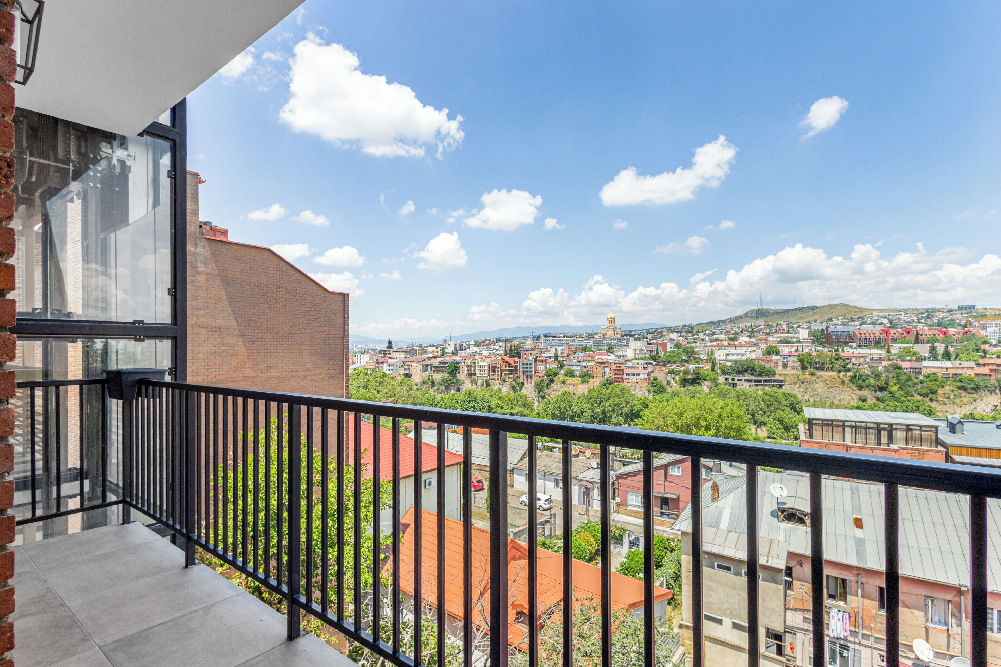 A balcony with a view of a cityscape, including buildings and greenery.
