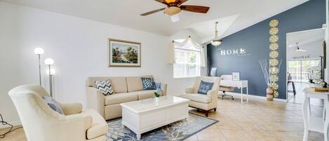 A living room with a beige sofa, a white coffee table, and a ceiling fan.