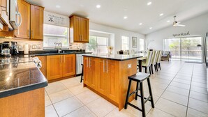 A modern kitchen with wooden cabinets, a central island, and bar stools. - 12 Mi to Disney: Family Home w/ Lanai in Davenport (Davenport)