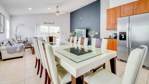 A modern kitchen with a stainless steel refrigerator, wooden cabinets, and a dining area with a glass-top table and chairs. - 12 Mi to Disney: Family Home w/ Lanai in Davenport (Davenport)
