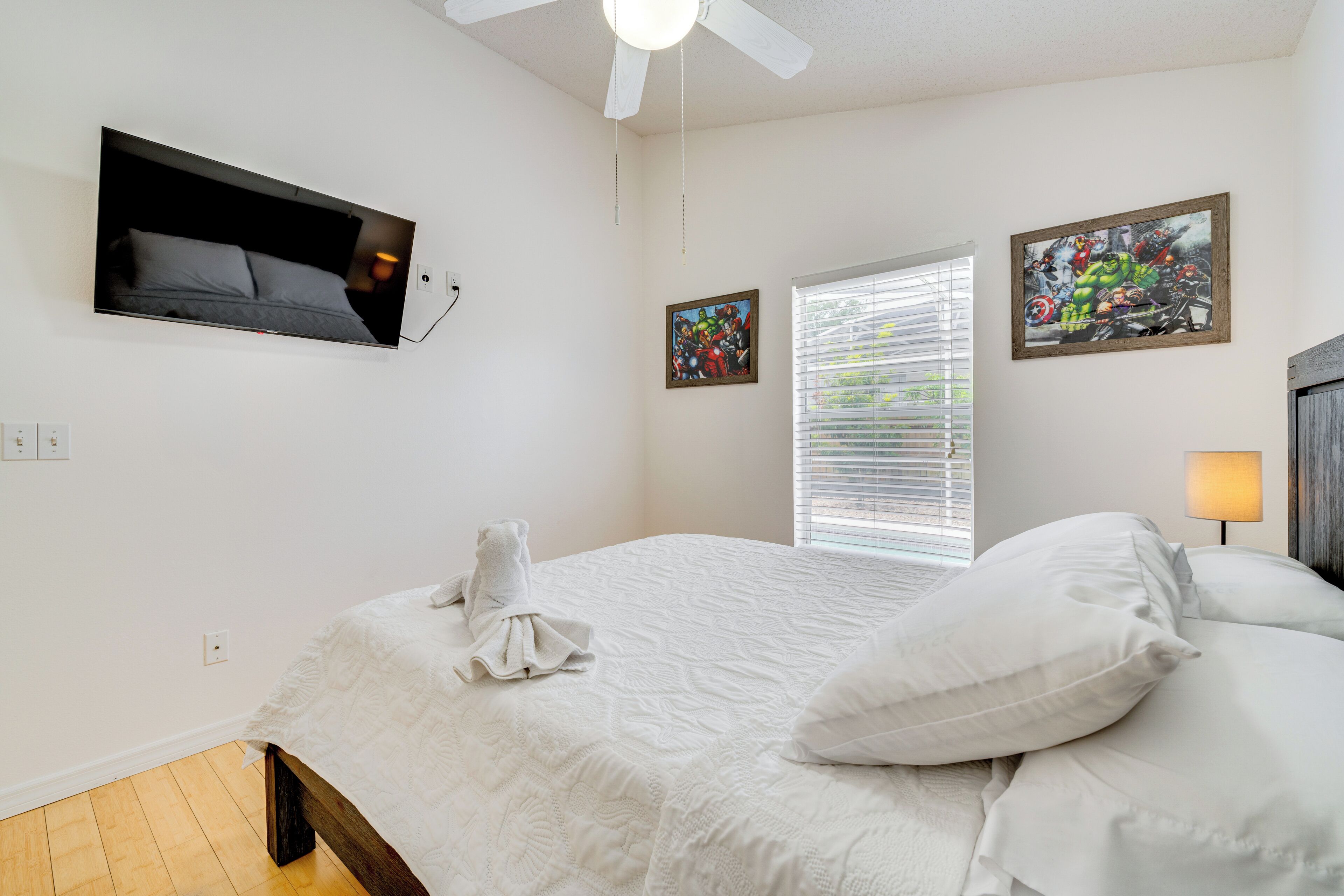 A bedroom with a bed, a ceiling fan, a TV mounted on the wall, and two framed pictures.