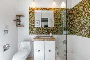 Une salle de bain moderne équipée de toilettes, d’un lavabo et d’une douche. On y trouve des étagères en bois ornées de plantes et un miroir au-dessus du lavabo.