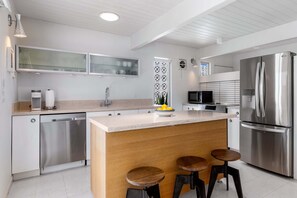 Une cuisine moderne dotée d’un îlot central, d’appareils électroménagers en acier inoxydable et de tabourets de bar.