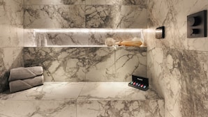 A bathroom with marble walls, a built-in shelf with toiletries, a towel, and a steam shower control panel. - The Sanctuary in Ullswater (Penrith)