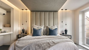 A modern bedroom with a large bed, two bedside tables, a nightstand, a window, and a built-in bench. - The Sanctuary in Ullswater (Penrith)