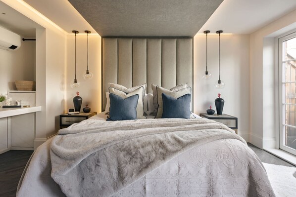 A modern bedroom with a large bed, two bedside tables, a nightstand, a window, and a built-in bench. - The Sanctuary in Ullswater (Penrith)