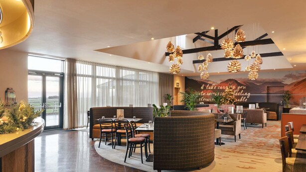 A spacious lobby with a curved seating area, a large window offering a view, and a ceiling with geometric light fixtures. - The Sanctuary in Ullswater (Penrith)