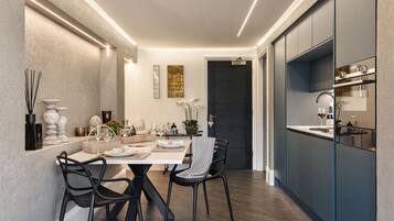 A modern kitchen with dark cabinetry, a dining area with a white table and black chairs, and a dark door in the background.