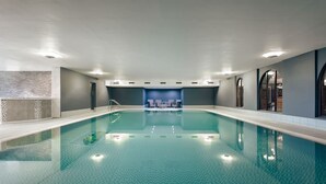 A large indoor swimming pool with a tiled floor and a seating area in the center. - The Sanctuary in Ullswater (Penrith)