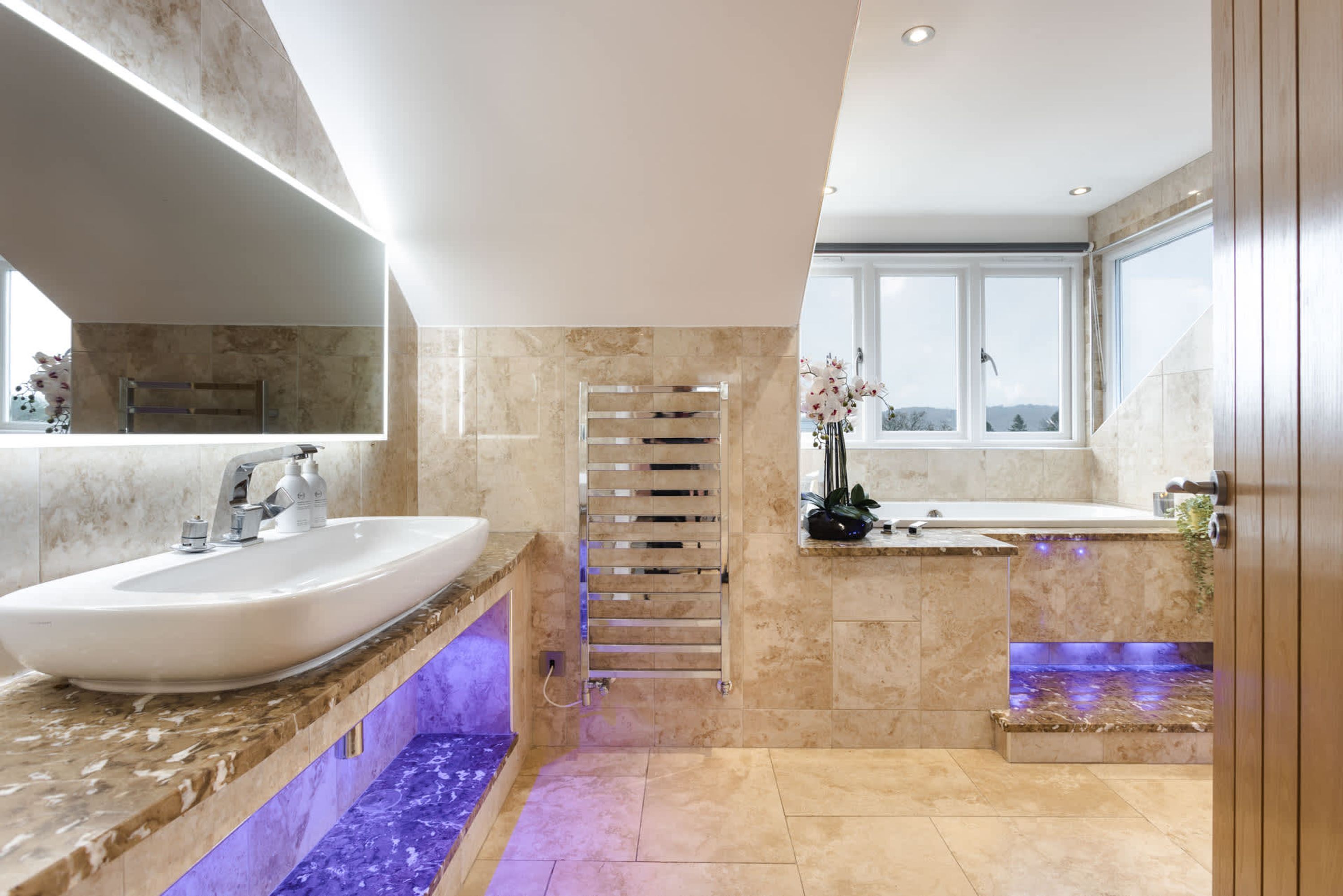 A modern bathroom with a large white sink, a glass shower enclosure, and a window providing a view of the outdoors.