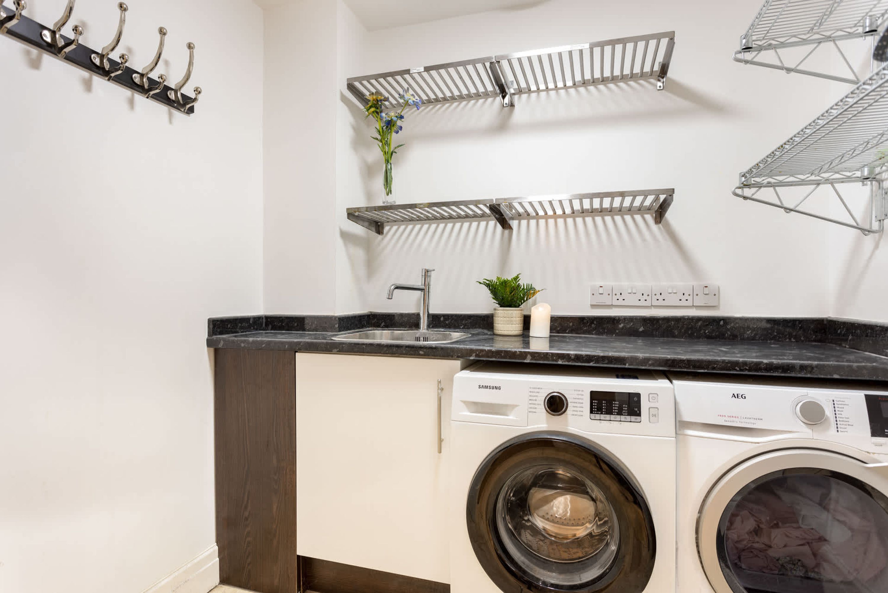 A laundry area with two washing machines, a sink, and metal drying racks.