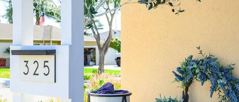 A building entrance with a white mailbox marked "325," a potted plant, and a small table with a chair.
