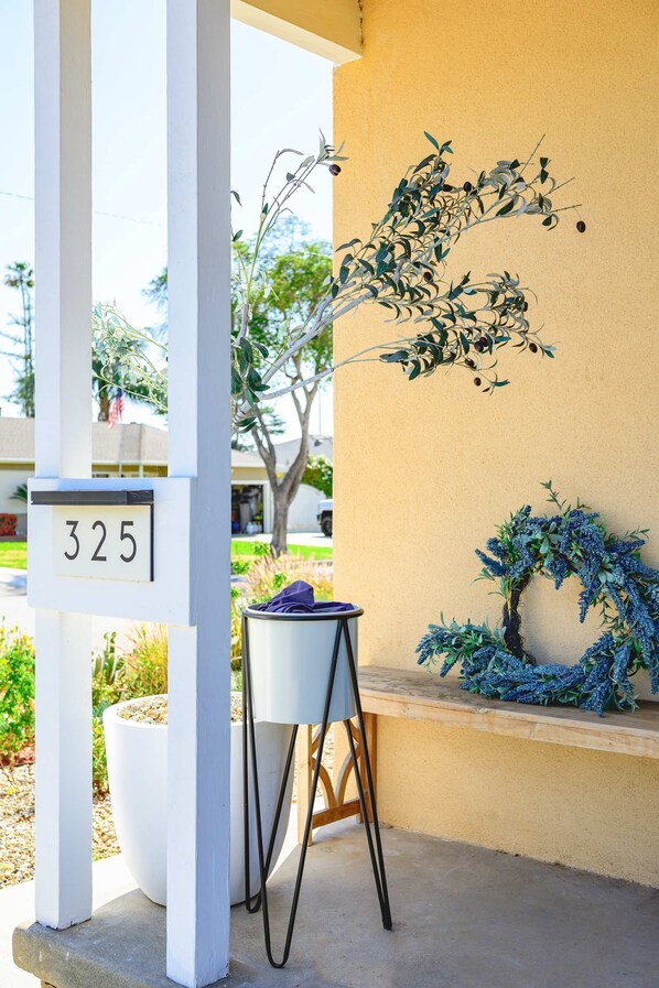 A building entrance with a white mailbox marked "325," a potted plant, and a small table with a chair. - Stylish New Home Bright Modern Fully Stocked (West Covina)