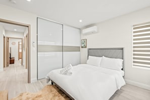 A modern bedroom with a large bed, a sliding door closet, and an air conditioning unit on the wall. - Stylish New Home Bright Modern Fully Stocked (West Covina)