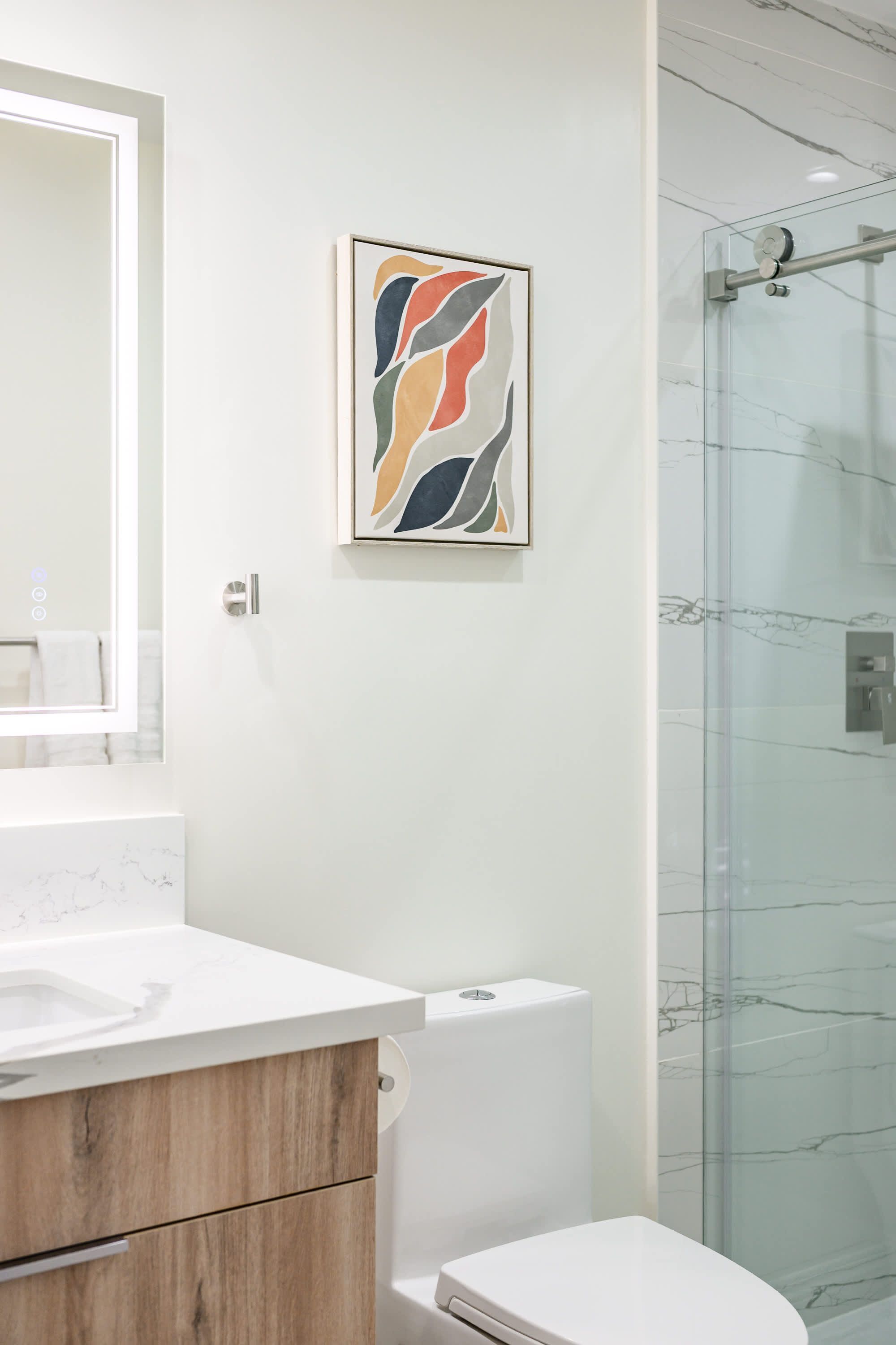 Une salle de bain moderne avec un meuble-lavabo blanc, un placard en bois, des toilettes et une cabine de douche en verre.