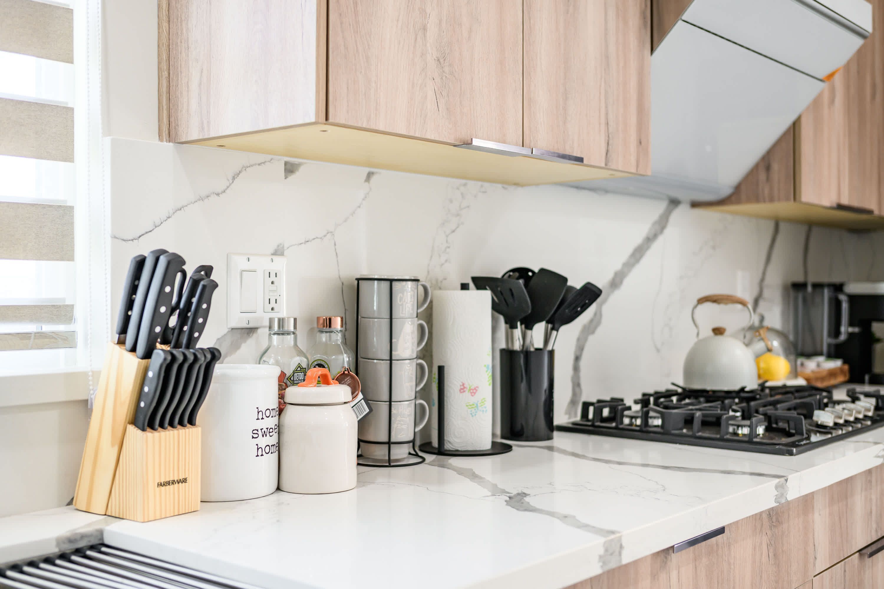 A modern kitchen with wooden cabinets, a marble countertop, and various kitchen utensils and appliances.